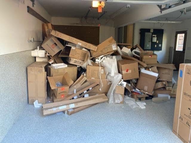 Piled cardboard boxes and packaging materials in a cluttered garage setting.