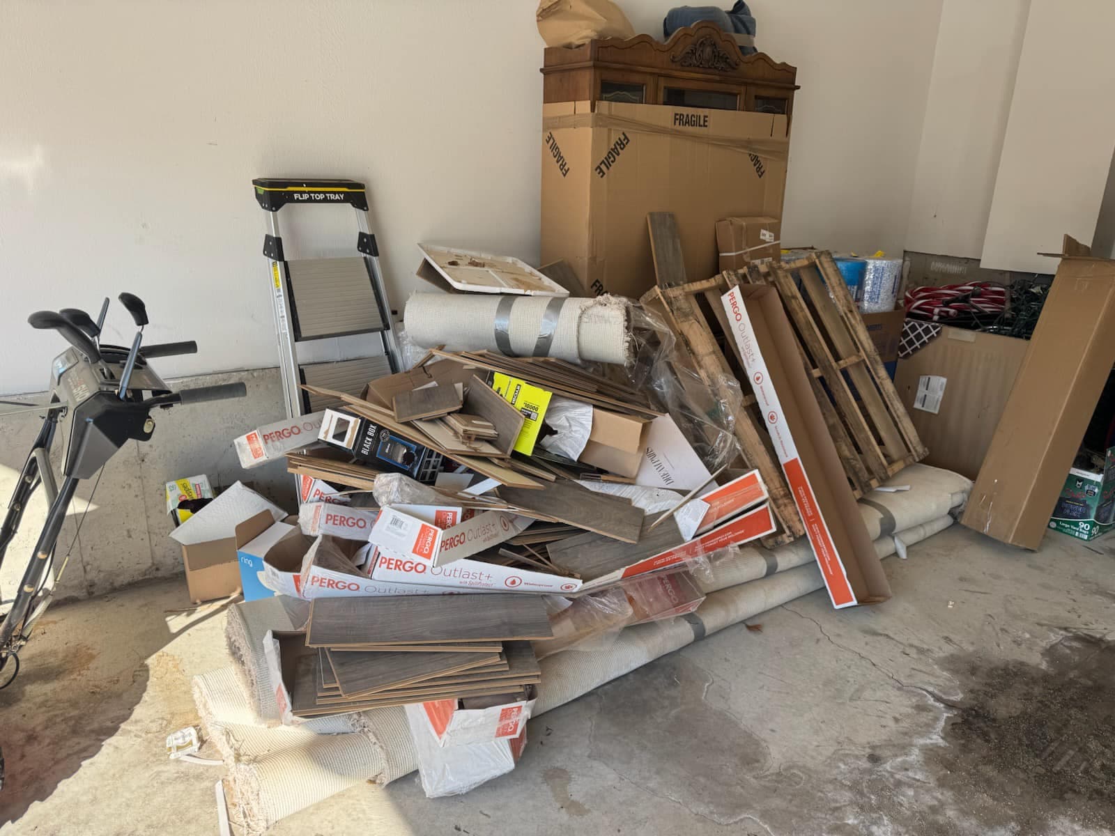 Cluttered garage with piles of boxes, cardboard, and construction materials.